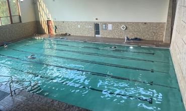 View of the indoor pool with light reflecting off the water from windows to the left side of the photo. The pool has swimming lanes. 